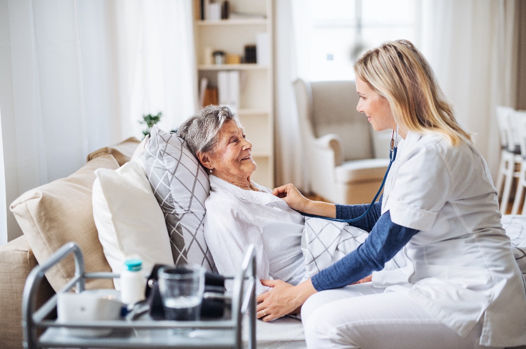 Eine Gesundheitsberaterin untersucht mit einem Stethoskop eine kranke ältere Frau, die zu Hause im Bett liegt.